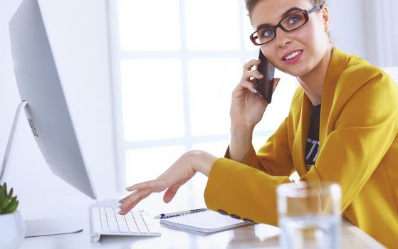 Businesswoman concentrating on work, using computer and cellphone in office