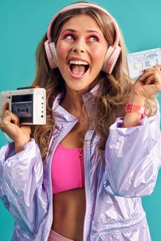 I have the greatest 80s hits on here. Studio shot of a young woman holding a cassette player while dressed in 80s clothing.
