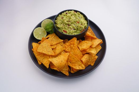 Top view of black plate of guacamole sauce or dip and tortilla chips or nachos isolated on a white background