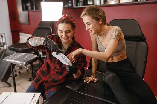 Young woman client choosing drawing in tattoo salon