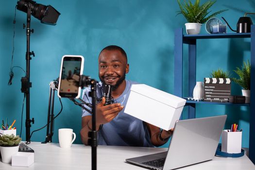 Smiling vlogger holding product box hosting online giveaway in front of recording smartphone