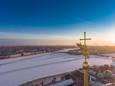Aerial view of golden Angel and Cross on spike of the Peter and Paul cathedral in Saint Petersburg at sunset, frozen Neva River, sunny frosty day, Winter Palace, Admiralty, Rostral columns