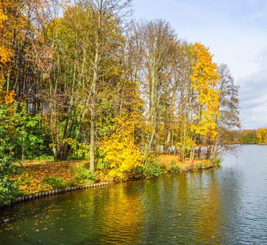 Autumn park with a beautiful lake on a sunny day. Bright colorful trees reflecting in the calm water of a lake