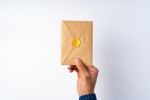 Male hand holding closed envelope above the white surface