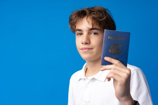 Portrait of glad handsome boy showing his passport going on vacation against blue background