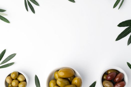 Bowl with green olives and olive leaves on white background