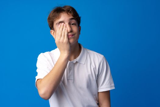 Sad teenager boy failed, touching face against blue background