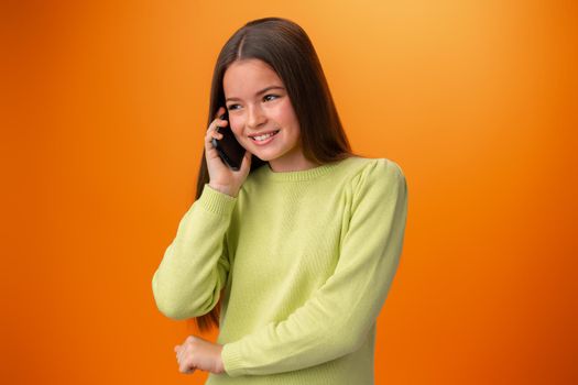 Teen girl talking on cell phone isolated on orange background