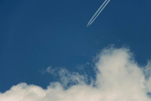 Airplane contrast against bright blue sky with a diagnonal straight condensation vapor trail, appearing as though it is heading towards a white candy floss cloud. Canon EOS 90D