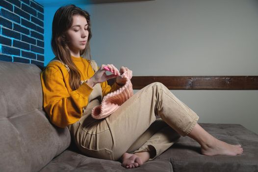 cute young caucasian woman sitting on sofa at home and crocheting wool product