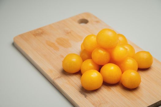 A heap of yellow cherry tomatoes on a wooden cutting board in the kitchen on a white table