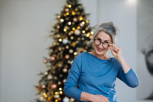 Elderly lady smiling and looking in camera, Xmas tree on background