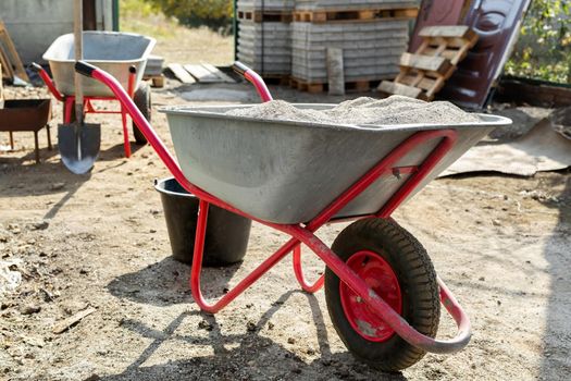 Construction wheelbarrow with cement and a shovel on the background of a stack of gray tiles