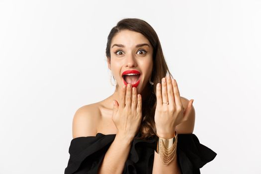 Excited woman showing engagement ring after saying yes to marriage proposal, bride looking excited, standing over white background