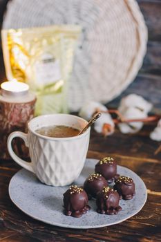 Dark chocolate handmade candy balls on handmade plate on dark wooden background with the cup of tea in a white cup