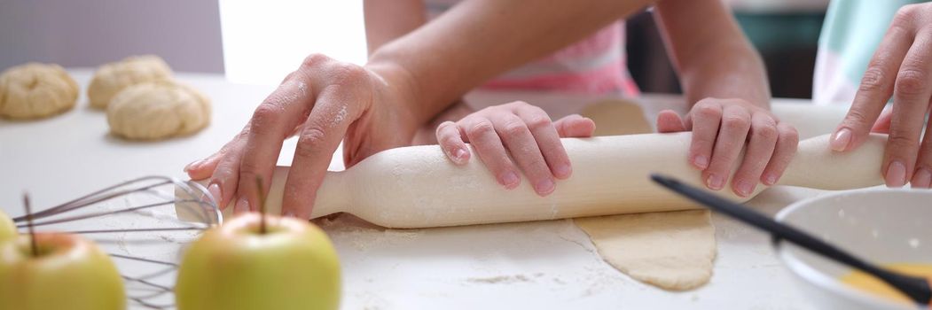 Adult and child roll out dough with rolling pin on table closeup