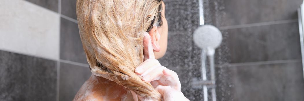 Woman washes hair with shampoo in shower closeup