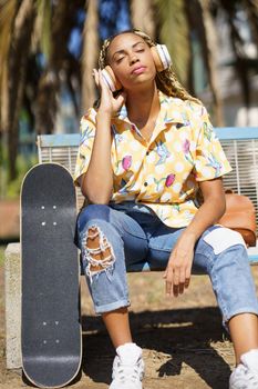 African girl with skateboard relaxing after riding skateboard listening to the music