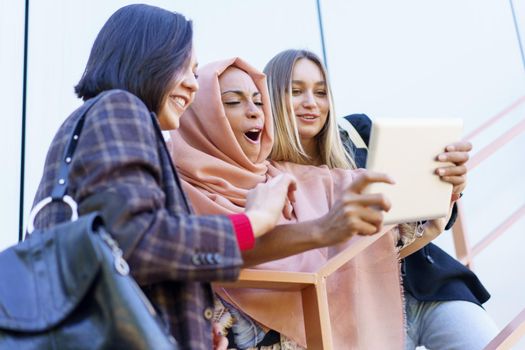 Smiling young diverse girls using tablet on stairs
