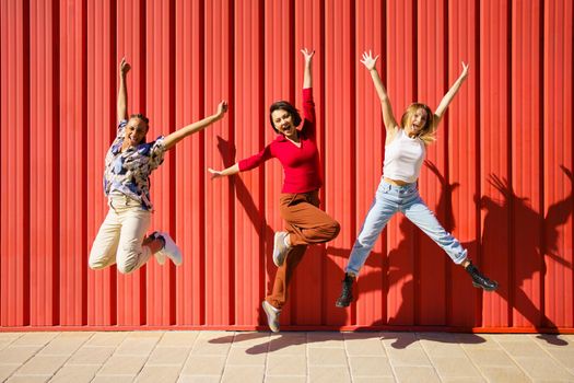 Cheerful diverse women jumping near wall