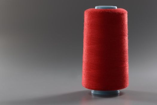 Red colour thread spool on grey background, yarn for sewing, bright thread for dressmaking