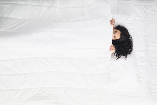 Woman laying on white bedding covering with blanket, wake up well rested in morning