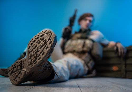 a male soldier in camouflage is sitting by an ammunition crate on the floor with a weapon