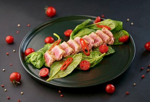 Cold appetizer of beef carpaccio with spinach and tomatoes on a black plate