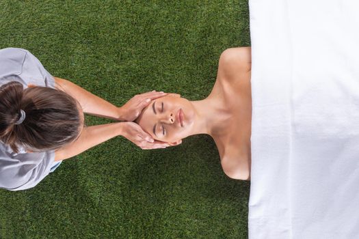 Woman at spa face massage procedures to clean the skin. top view shot. Green grass background