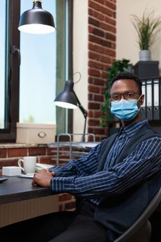 Portrait of successfull startup employee with covid face mask sitting at desk