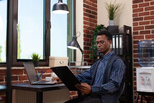 Startup employee holding clipboard with bussiness charts sitting at desk comparing data