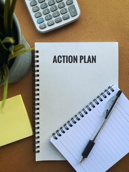 Image with action plan text on a note pad with pen, plant, calculator and sticky note.