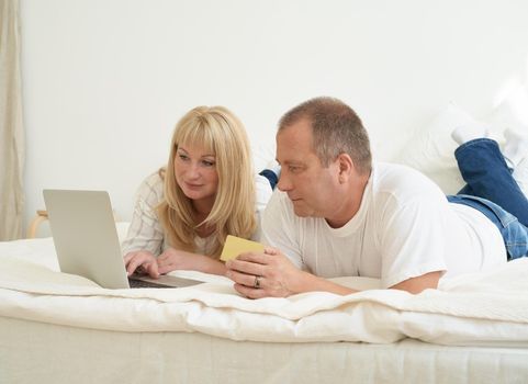 Mature family couple sitting at bed in modern home, looking at laptop screen.