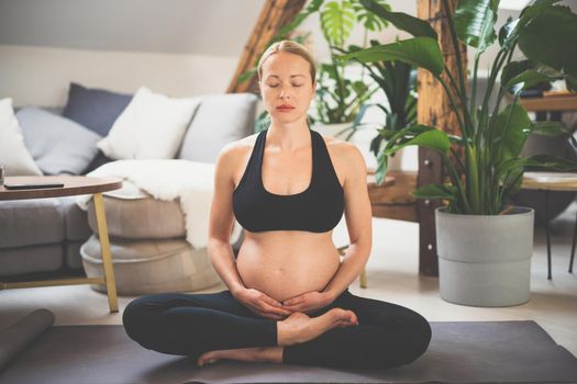 Young beautiful pregnant woman training yoga, caressing her belly. Young happy expectant relaxing, thinking about her baby and enjoying her future life. Motherhood, pregnancy, yoga concept.