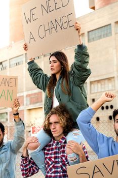 Young hispanic woman sitting on mans shoulder protesting against climate change in demonstration. Vertical image.