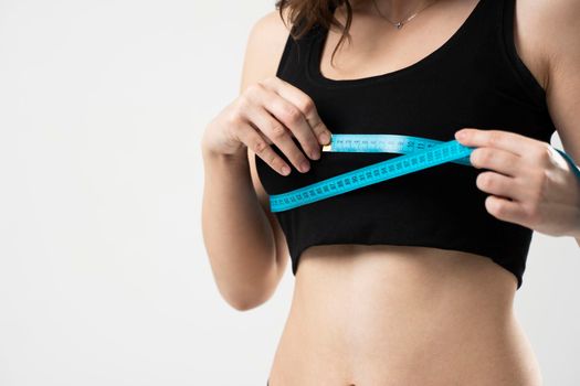 Beautiful sporty slim young woman measuring her figure size with tape measure. Womans holding centimeter and measuring a breasts with a blue measure tape.