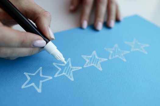 Woman hand painting over stars on blue paper for evaluating work closeup
