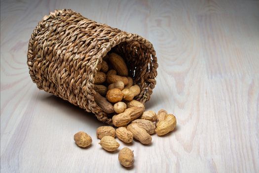 Shelled peanuts in a small wicker basket on a white background. Peanuts full from a wicker basket. Peanuts spill out of a wicker basket.