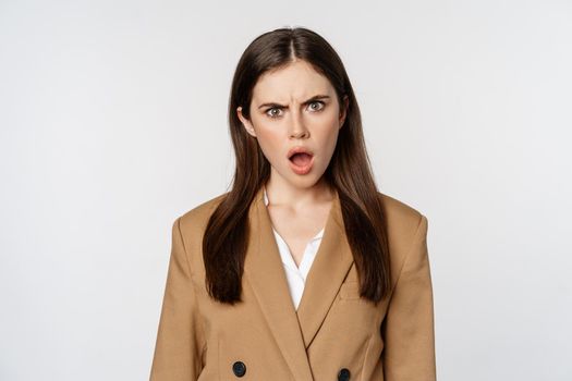 Frustrated, insulated woman in business outfit, staring startled and shocked at camera, standing over white background