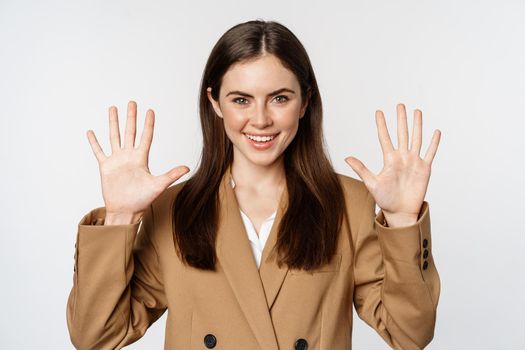Portrait of corporate woman, saleswoman showing number ten fingers and smiling, standing in suit over white background