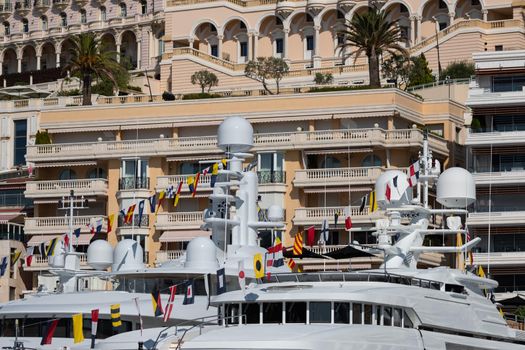 A lot of huge yachts are in port of Monaco at sunny day, Monte Carlo, real estate housing is on background, glossy board of the motor boat, megayachts are moored in marin