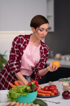 Young pretty housewife with a bob hairstyle prepares food in the kitchen choosing tomato red or yellow. Healthy food at home. Healthy food leaving - vegan concept