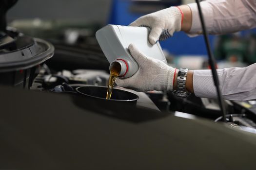 Man in gloves refueling and pour new fresh oil into engine motor car