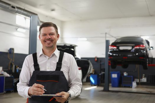 Smiling qualified maintenance center worker in uniform, man posing on cars background at work