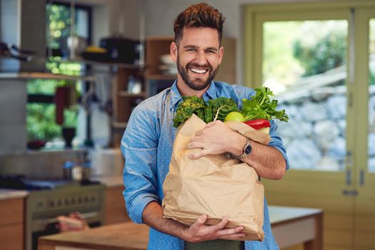 Living healthy, living well. Portrait of a happy man holding a bag full of healthy vegetables at home.