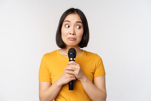 Modest asian girl holding microphone, scared talking in public, standing against white background