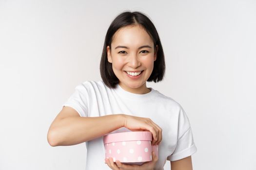 Happy asian woman, girlfriend open box with valentines day gift, receive romantic present, standing over white background