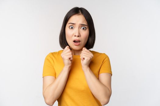 Portrait of scared asian woman shaking from fear, looking terrified and concerned, standing anxious against white background