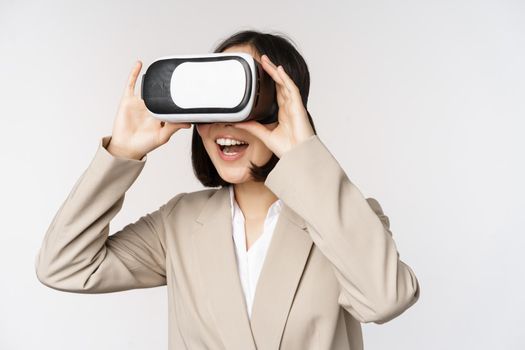 Amazed business woman in suit using virtual reality glasses, looking amazed in vr headset, standing over white background