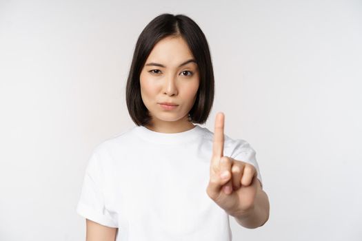Image of asian girl showing stop, prohibit smth, extend one arm to show forbidding, taboo gesture, standing in tshirt over white background
